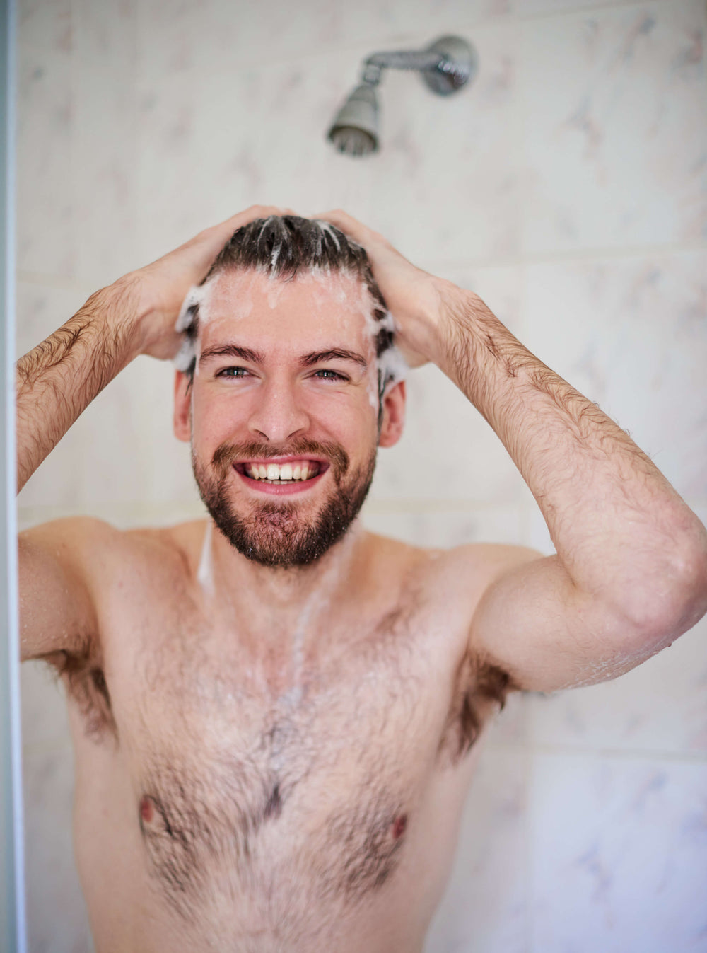 Man smiling while washing his hair in the shower